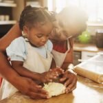 Black woman, child and teaching with dough, cooking and nutrition for support, love and education. Grandmother, girl and baking for development, growth and kitchen as happy family in bonding in home