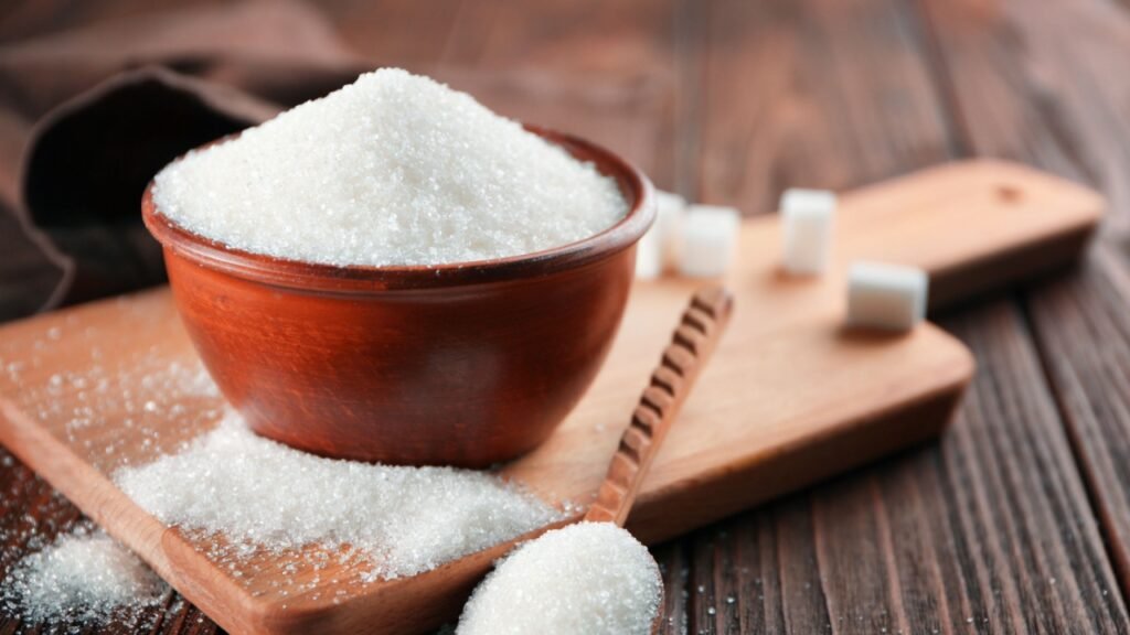 Bowl and spoon full of sugar on wooden background