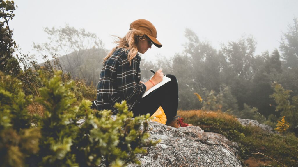 woman-sitting-on-top-of-a-rock-writing-WA_O4UAUfxc