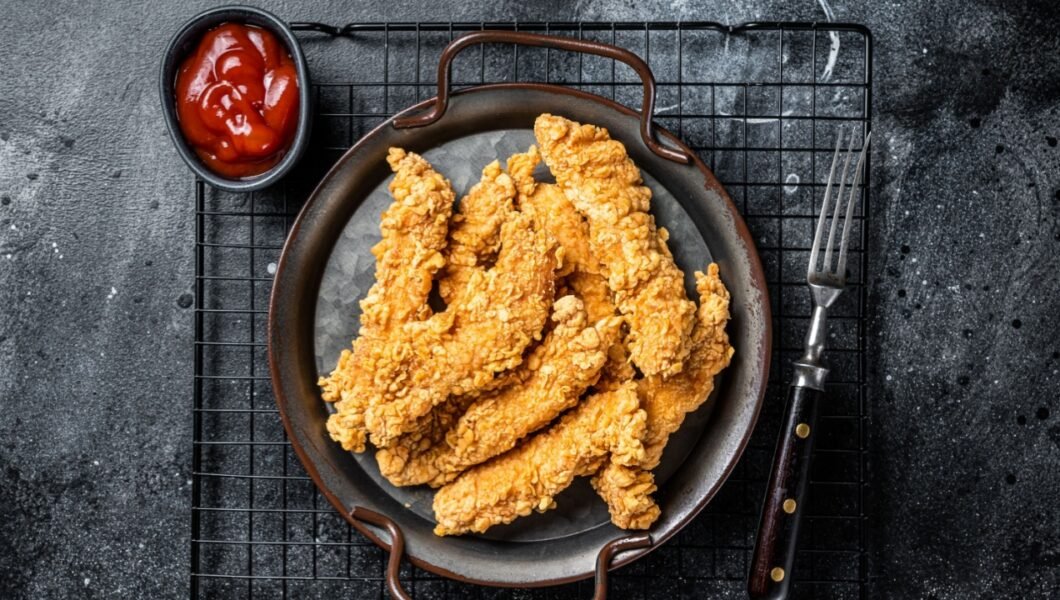 Crispy chicken tenders strips with Ketchup. Black background. Top view.