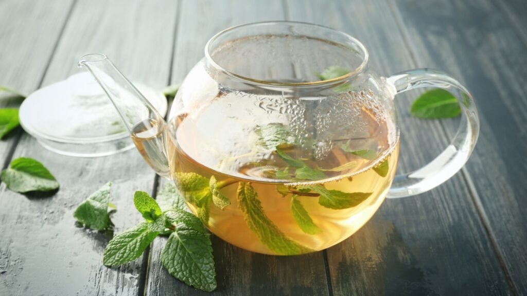 Glass teapot with hot tasty lemon balm tea on wooden table