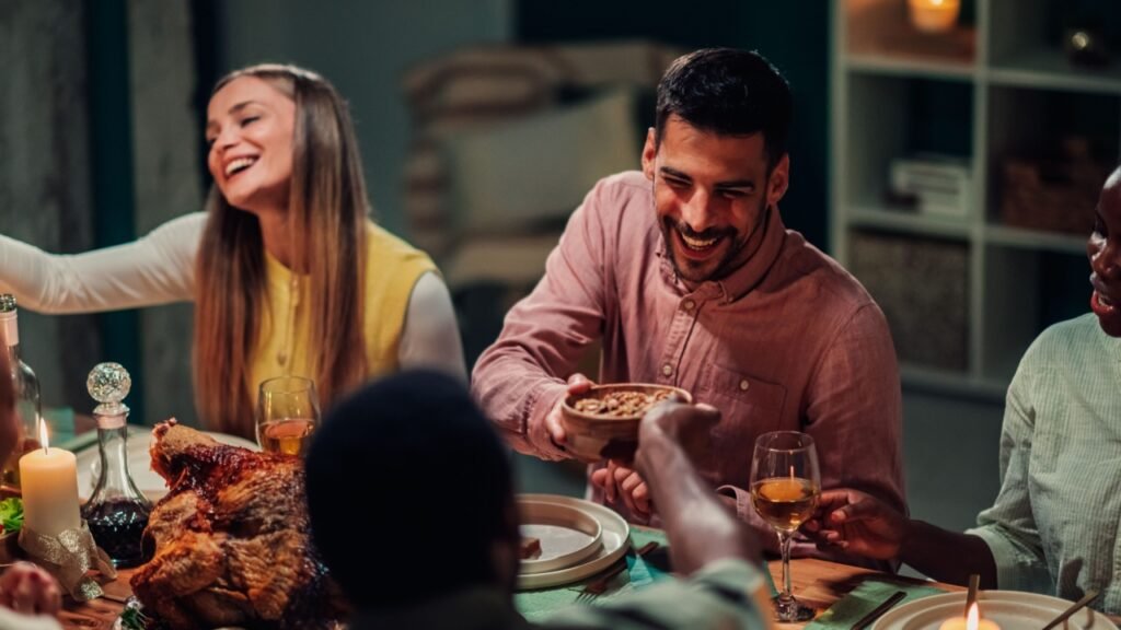Happy friends sharing a festive thanksgiving dinner, laughing and enjoying delicious food while celebrating together in a warm, cozy atmosphere