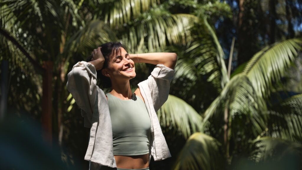 Happy relaxed young Hispanic woman enjoying summer sunny day with eyes closed feeling no stress, peace of mind, mental balance relaxing standing in green nature park among tropical trees.