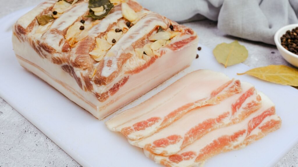 Homemade salted pork fat with garlic, bay leaves, pepper and cherry tomatoes. Rustic food composition on kitchen table.