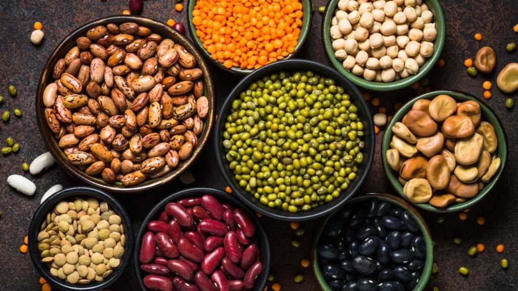 Legumes, lentils, chikpea and beans assortment in different bowls on stone table. Top view.