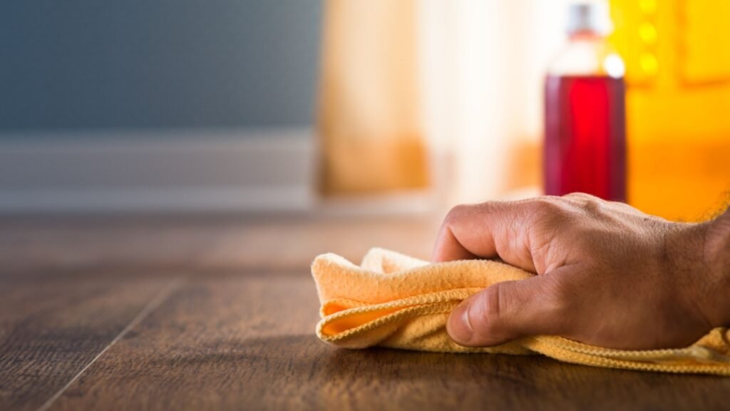 Male hand applying wood care products and cleaners on hardwood floor surface.