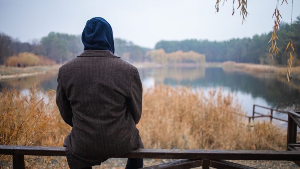 A young man sits alone by the lake in cloudy foggy morning. To be alone with yourself.