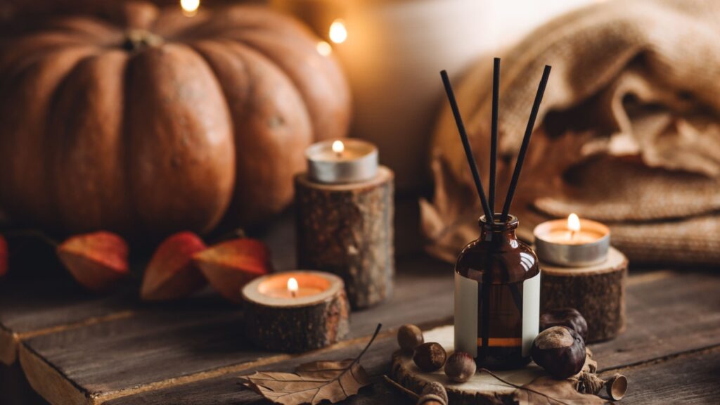 Autumn cozy mood composition with burning candles. Aroma stick reed diffuser, pumpkin on wooden table, knitted warm plaid. Fall hygge home decor, aromatherapy. Relaxed atmosphere in the apartment