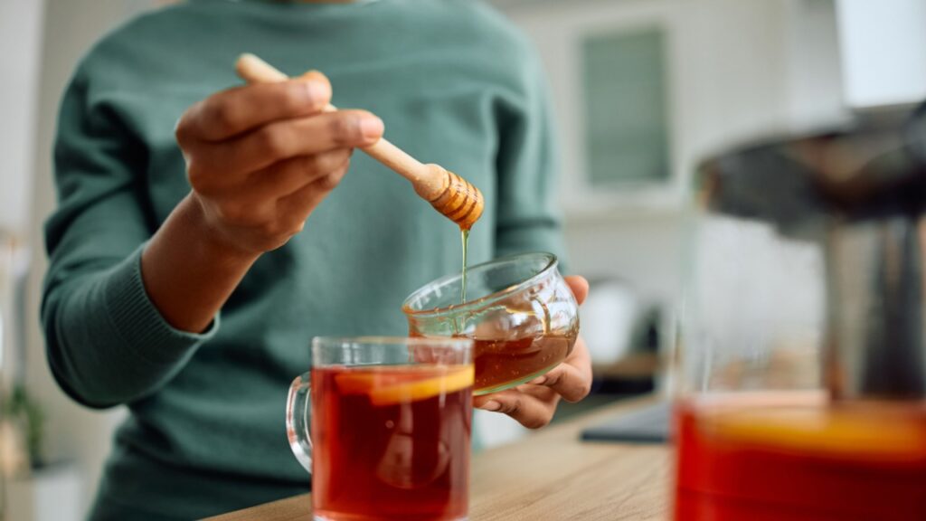 Close up of African American woman making tea with honey at home.