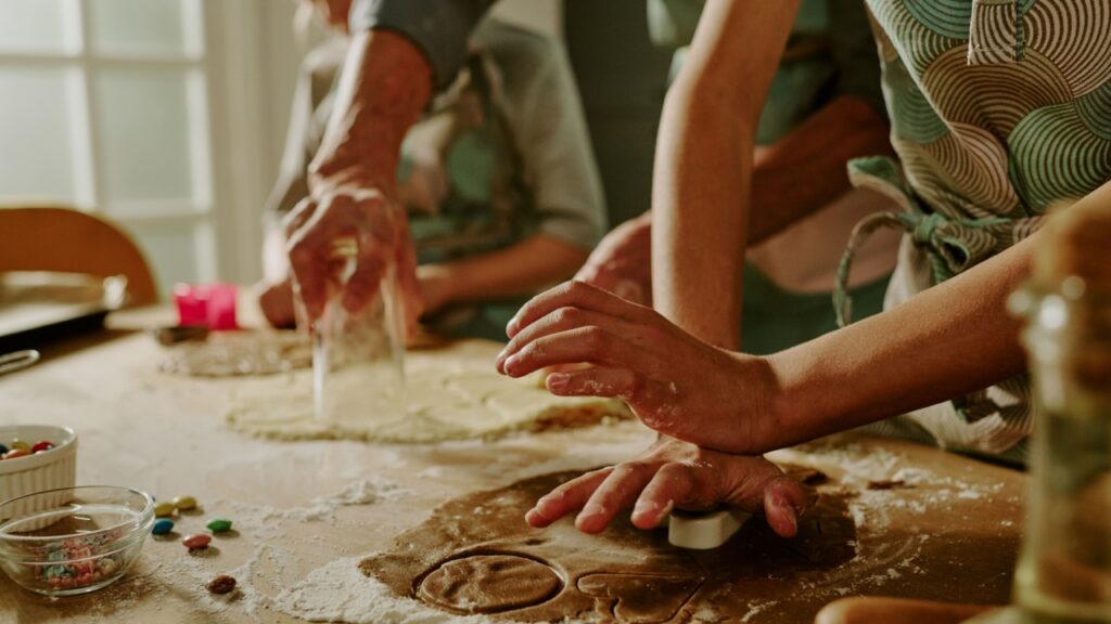 Close-up of family baking cookies together, hands busy with rolling and cutting dough on a kitchen counter, showing teamwork, joy, and love in the process of cooking