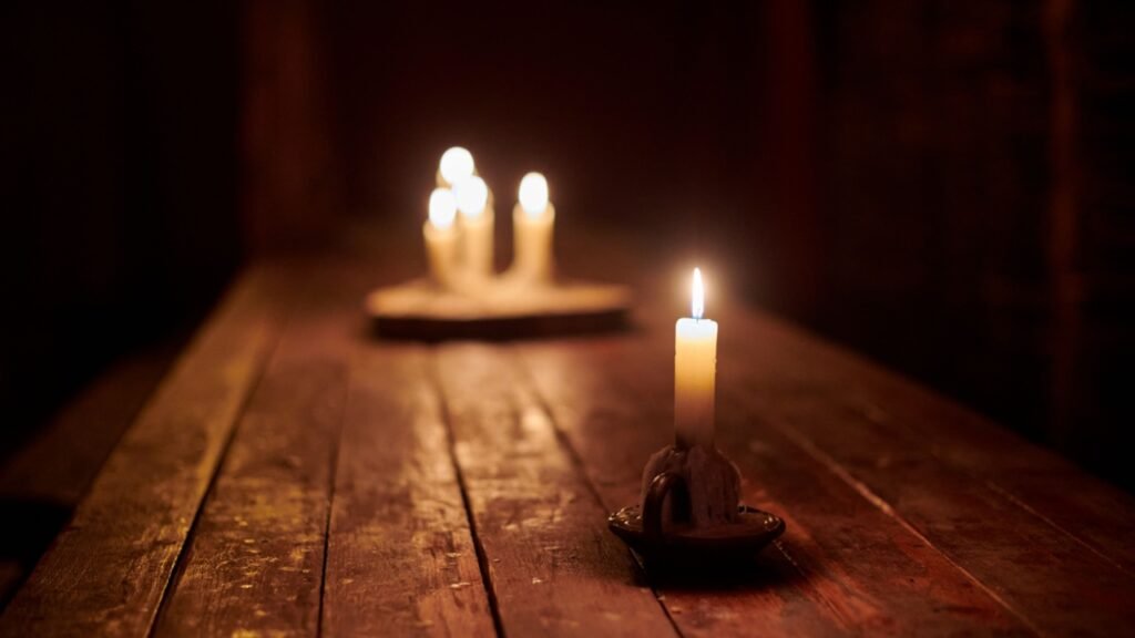 Four lit candles on wooden base illuminate rustic table in dark, cozy and peaceful atmosphere. Candle on old tavern table evoking charm of an old tavern cozy, tranquil ambiance