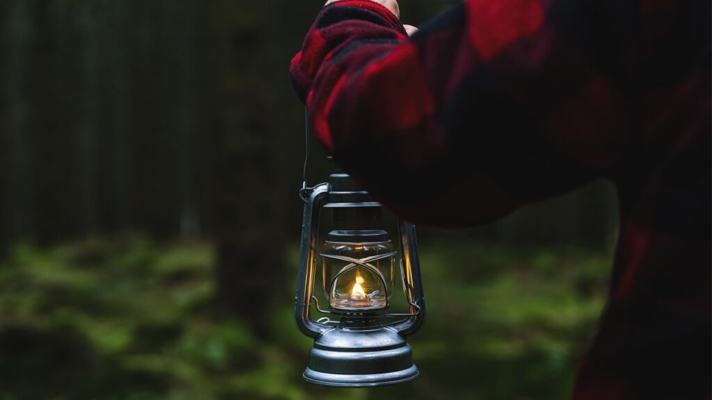 Hiker holding a oil lantern or kerosene lamp and walking in the dark forest