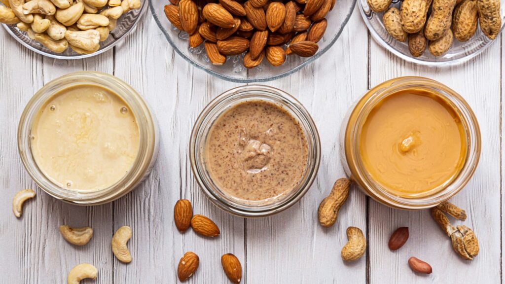 Modern concept of wellness and veganism. Jars of almond, cashew and peanut butter on a white wooden table. Organic, homemade nut butter for a healthy breakfast.