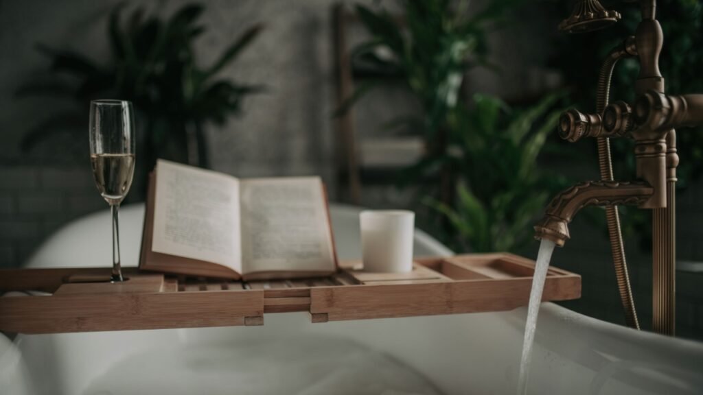 Native hues organic shapes look of bathroom with big window oval bathtub in neutrals earth tones. Green palm plants candles bubblebath leasure and relaxation skin selfcare wellness luxury living