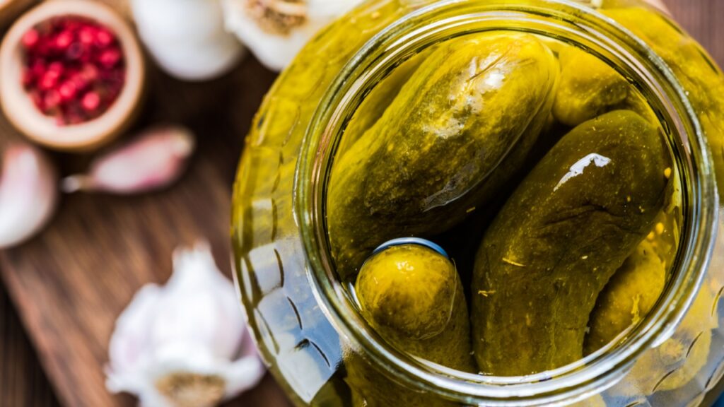 Pickled gherkins in jar, fermented food with spices, view from overhead on wooden table
