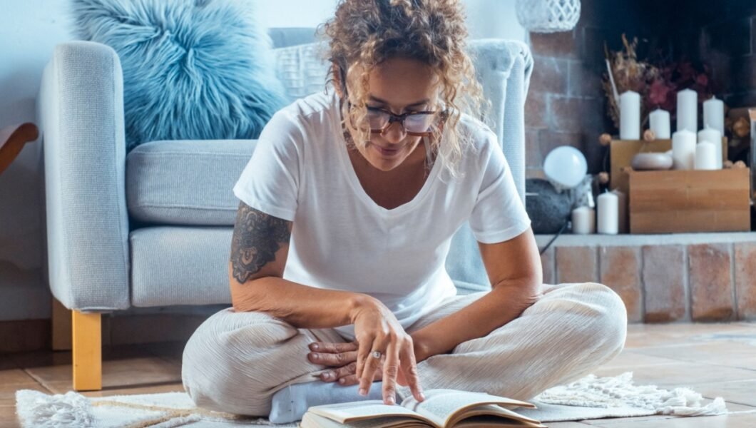 Relaxed woman sitting indoors on a peaceful afternoon, wearing glasses and reading a book, surrounded by a cozy and serene home environment while enjoying a calm moment of solitude
