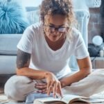 Relaxed woman sitting indoors on a peaceful afternoon, wearing glasses and reading a book, surrounded by a cozy and serene home environment while enjoying a calm moment of solitude