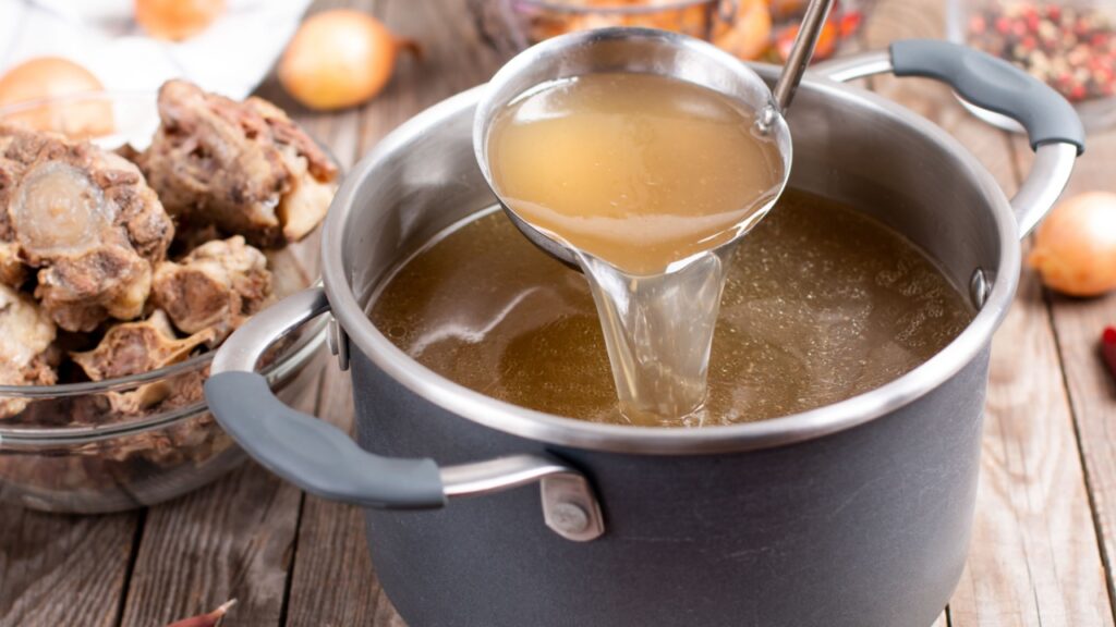Saucepan with bouillon with a ladle on the table. Bone broth