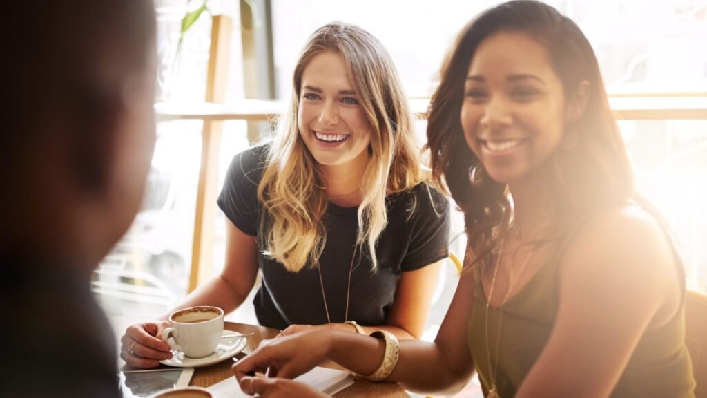 Smile, group and friends drinking coffee in shop for talking, conversation or social gathering together in restaurant. Happy women, students and relax in cafe for chat, news or laughing gossip story