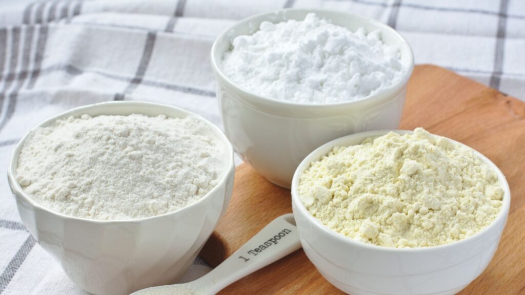 Three bowls with gluten free flour - rice flour, millet flour and potato starch and spoon with xanthan gum