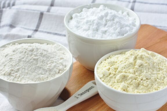 Three bowls with gluten free flour - rice flour, millet flour and potato starch and spoon with xanthan gum