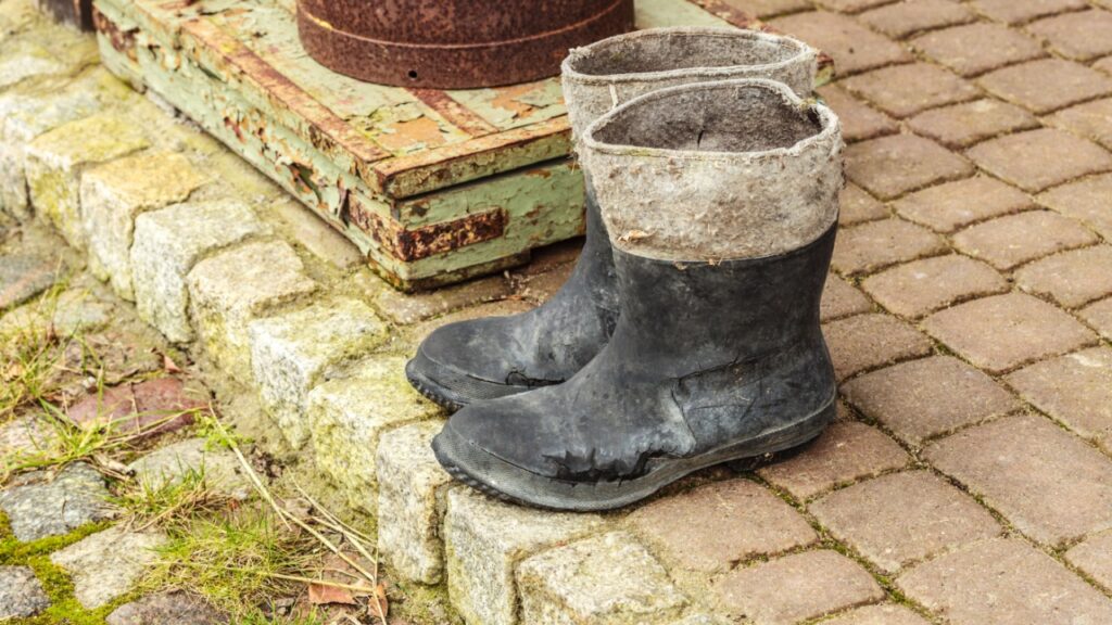 Village detailed objects concept. Very old wellingtons and copper bottle standing outside