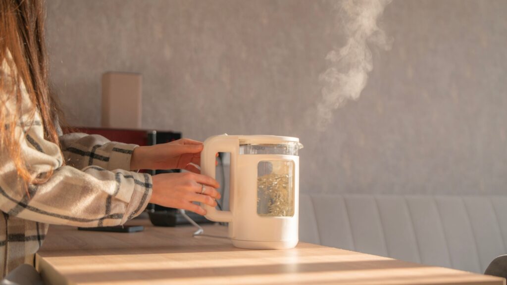 Water boils in an electric kettle as steam escapes, creating a warm atmosphere in a well-lit indoor space during the day.