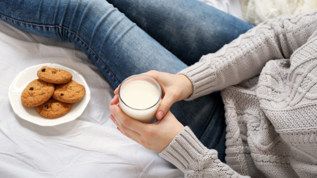 Woman drinking milk with cookies on her bed
