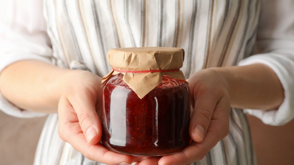 Woman holds glass jar with strawberry jam, close up