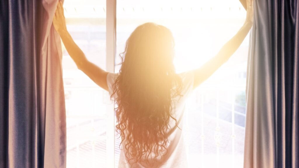 Woman opens the curtains in the morning in the bedroom.  Sunlight shines into the room. Concept of  new day beginning. Blurred photo with soft focus. 
