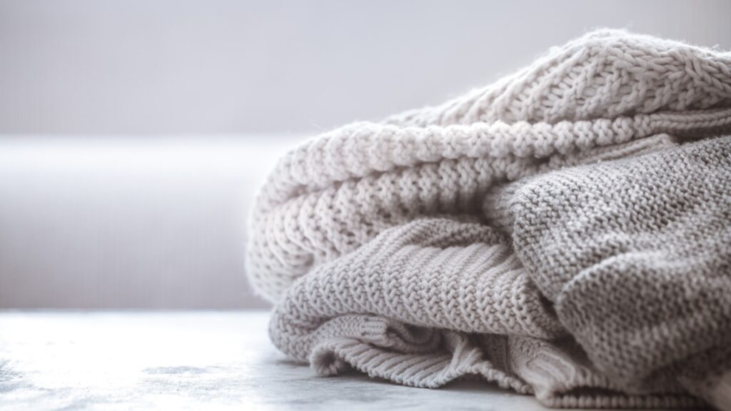 knitted sweaters on a wooden background, space for text